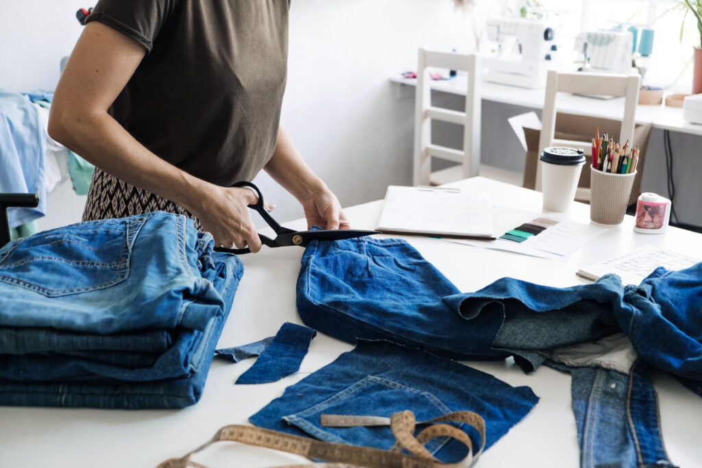 Reuse, repair, upcycle. Sustainable fashion, Circular economy. Denim upcycling ideas, repair and using old jeans. Close-up of old denim jeans fabric stack in Sewing studio.